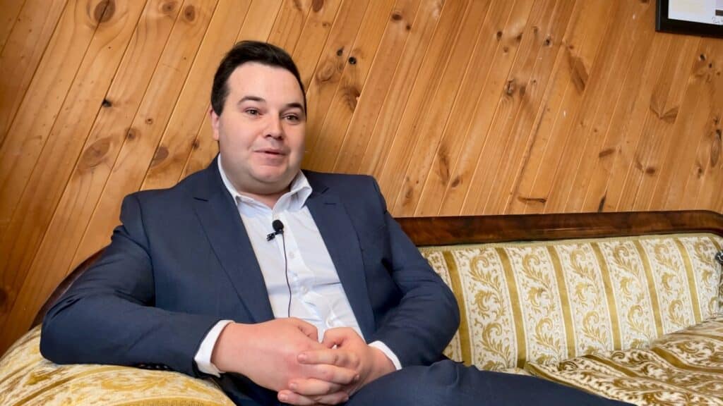 Ben Dudman sitting on a couch with timber panelling behind him.