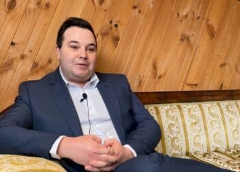 Ben Dudman sitting on a couch with timber panelling behind him.