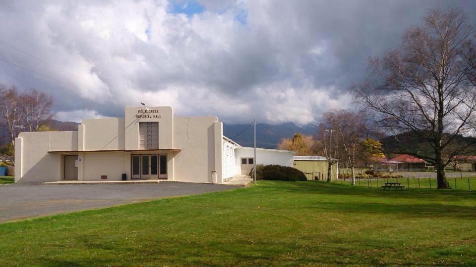 Mole Creek Market hall with green grass at the front and a dark and cloudy sky behind the white art deco hall