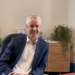 PJS Financial web with Sam Horsman sitting behind his desk in his office. He is sitting on an office chair and leaning to the side, with a potplant on the cupboard behind him.
