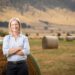 Rebecca White on her family farm with round hay bales on the field behind her.