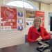 Jenny Irving dressed in bright red at the Westbury Post Office front counter.