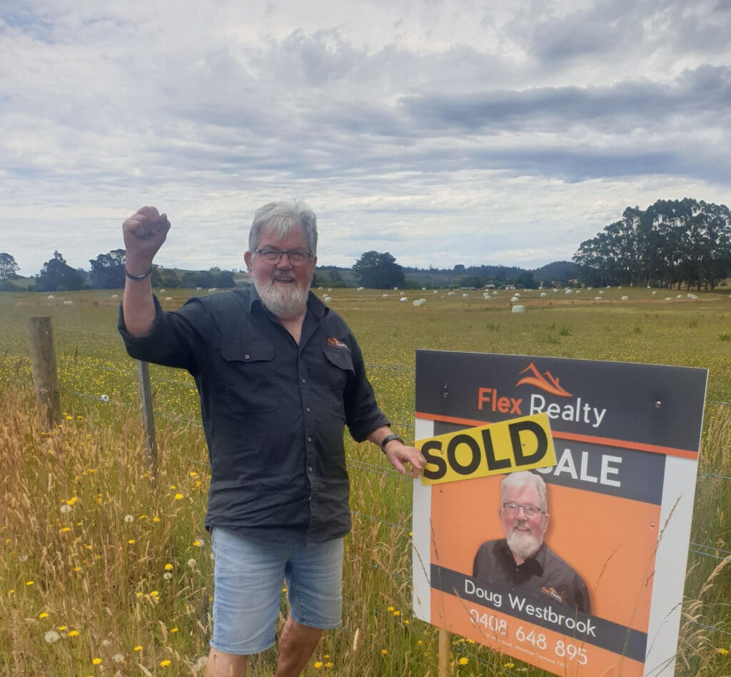 Doug Westbrook standing in front of a sold sign on a rural fence with a paddock behind.