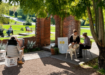 arts deloraine of the yellow share chair project. A couple of people talk while sitting in a garden in Deloraine.